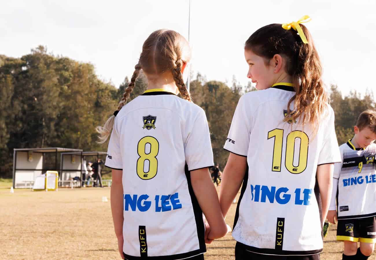back of 2 young female football players in the minis program holding hands